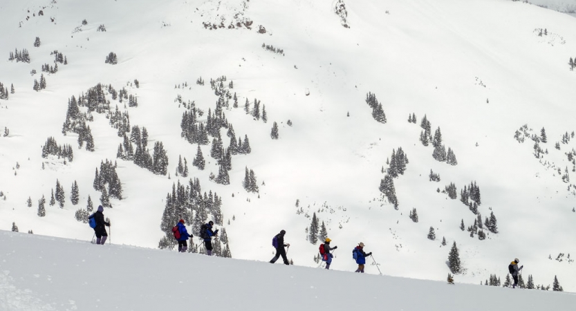 A group of people wearing winter gear hike in a line in a mountainous snowy landscape.